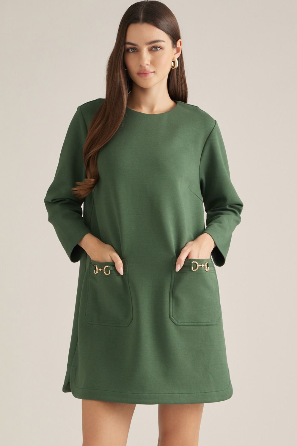 Solid long sleeve mini dress with a round neckline. Back zipper. Front pockets with gold-tone buckle detail